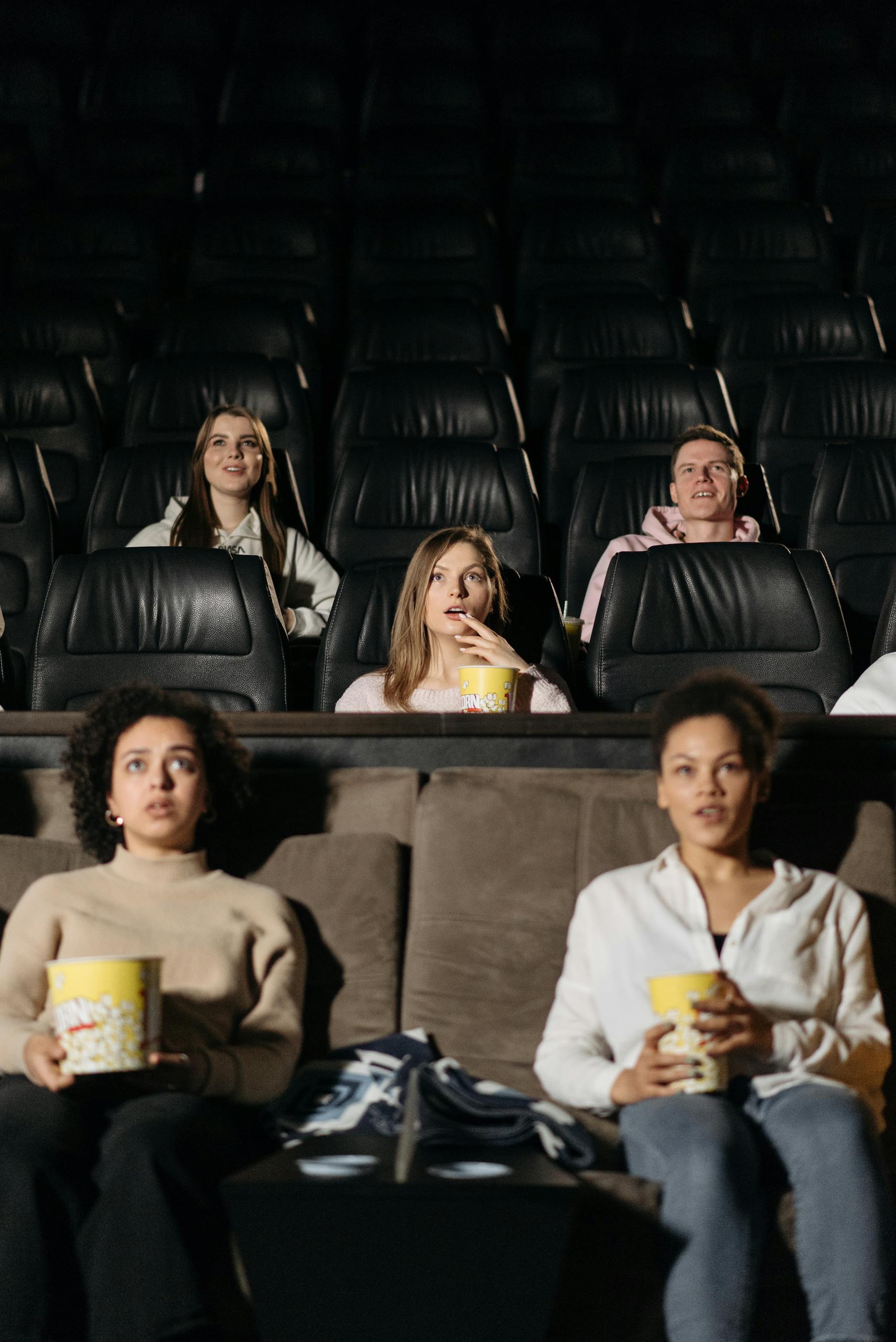 Audience watching film in theater, enjoying popcorn in a cozy setting.